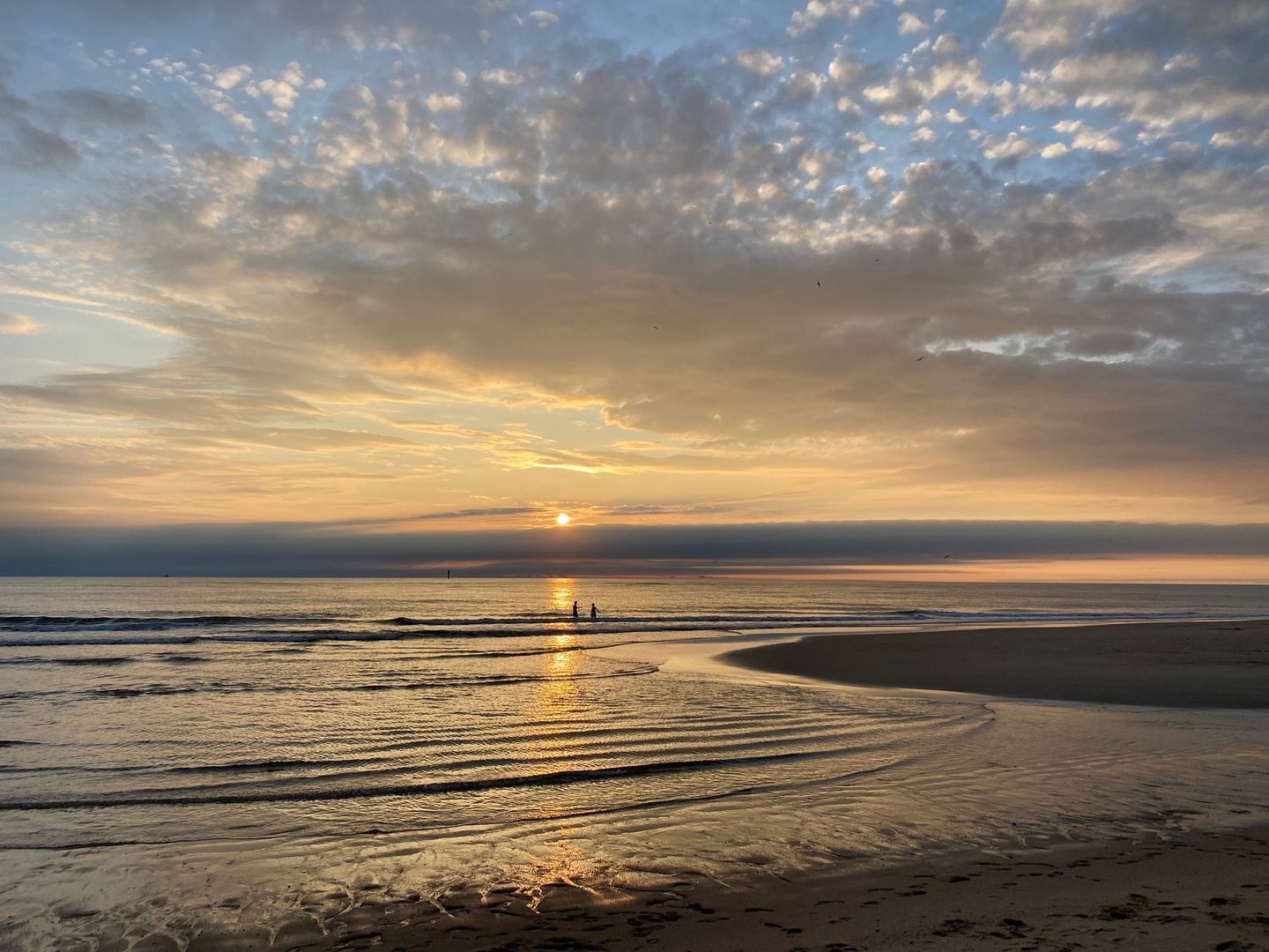 Une plage au coucher du soleil, avec des vagues et des empreintes de pas.