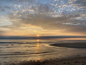 Une plage au coucher du soleil, avec des vagues et des empreintes de pas.