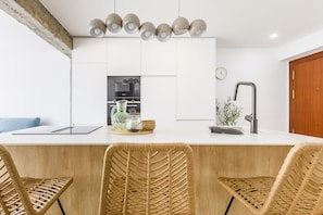 Et moderne køkken med en central ø, barstole, indbygget ovn og en hængende lampe.