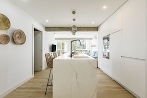 Une cuisine moderne dotée d’un îlot en marbre, de meubles blancs et d’un luminaire suspendu.