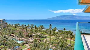 A resort with a pool area surrounded by palm trees, overlooking a beach and ocean with a mountain in the distance. - Maui Resort Rentals: Honua Kai - Premier 7th Floor Penthouse, 4BR w/ Stunning Ocean and Black Rock Views! (Lahaina)