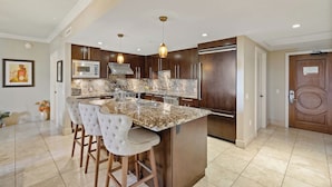 A modern kitchen with dark wood cabinets, a marble countertop, and a central island with bar stools. - Maui Resort Rentals: Honua Kai - Premier 7th Floor Penthouse, 4BR w/ Stunning Ocean and Black Rock Views! (Lahaina)