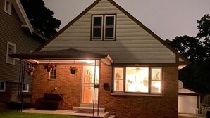 A two-story house with a brick facade, a front porch, and a well-lit entrance. - Ultra Clean, Private, Comfy Home in Prime Location. Sleeps up to 8. (Milwaukee)