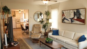 A living room with a sofa, armchair, coffee table, and a television. There is a kitchen in the background with cabinets and a refrigerator. - Ultra Clean, Private, Comfy Home in Prime Location. Sleeps up to 8. (Milwaukee)