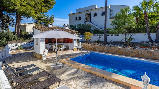 A pool area with lounge chairs, a covered seating area, and a stone wall.