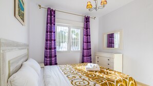 A bedroom with a bed, a dresser, a mirror, and purple curtains.