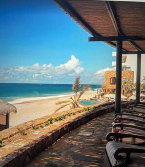 Relax on the beachfront patio with a shaded seating area overlooking the ocean and palm trees.