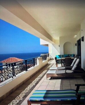 Relax on the balcony with a view of the sea, featuring comfortable lounge chairs and a small table.
