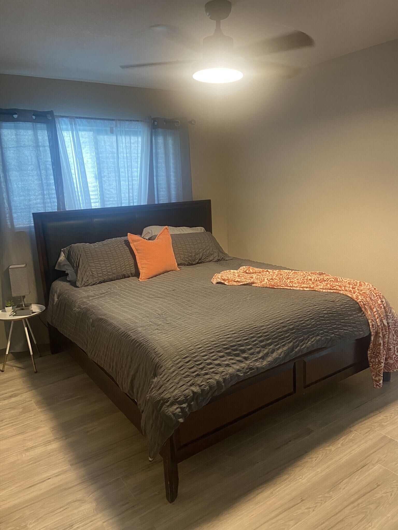 A bedroom with a bed, a nightstand, a lamp, a ceiling fan, and a window with curtains.