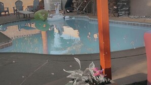 En pool med ett klart vatten som speglar omgivningen, omgiven av utemöbler och en krukväxt.