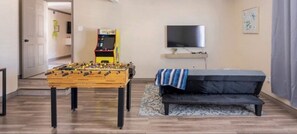 Una sala de estar con mesa de futbolín, sofá, televisor y una mesita con una planta.