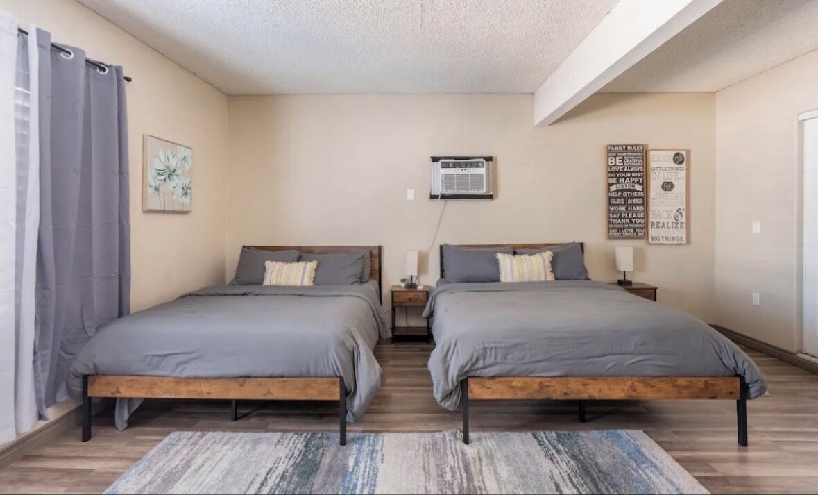 Une chambre avec deux lits, un ventilateur de plafond, un appareil de climatisation et une citation inspirante sur le mur.