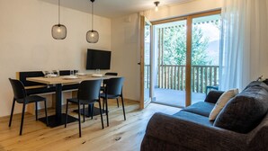 Una sala de estar moderna con un sofá, una mesa de comedor con sillas y un televisor montado en la pared.