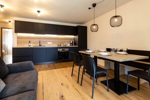 Une cuisine moderne avec des meubles de couleur sombre, un plan de travail en bois et un coin repas comprenant une table et des chaises.