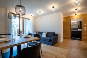A modern living room with a wooden floor, a dining table set for four, and a blue sofa. - Casa Erika in quiet area near Plan de Corones (Santo Stefano)