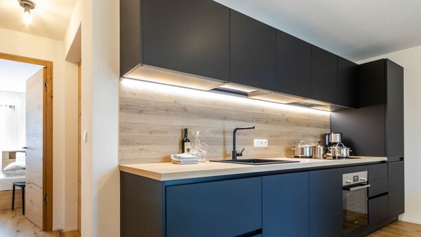 Una cocina moderna con armarios oscuros, encimera de madera y electrodomésticos integrados.