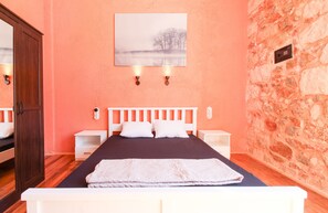 Een slaapkamer met een houten bed, witte nachtkastjes, een stenen muur en een schilderij van een landschap.