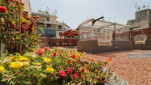 A rooftop garden with colorful flowers, a wooden pergola, and hanging macrame chairs. - Modern apartment with roof terrace in Athens (Athens)