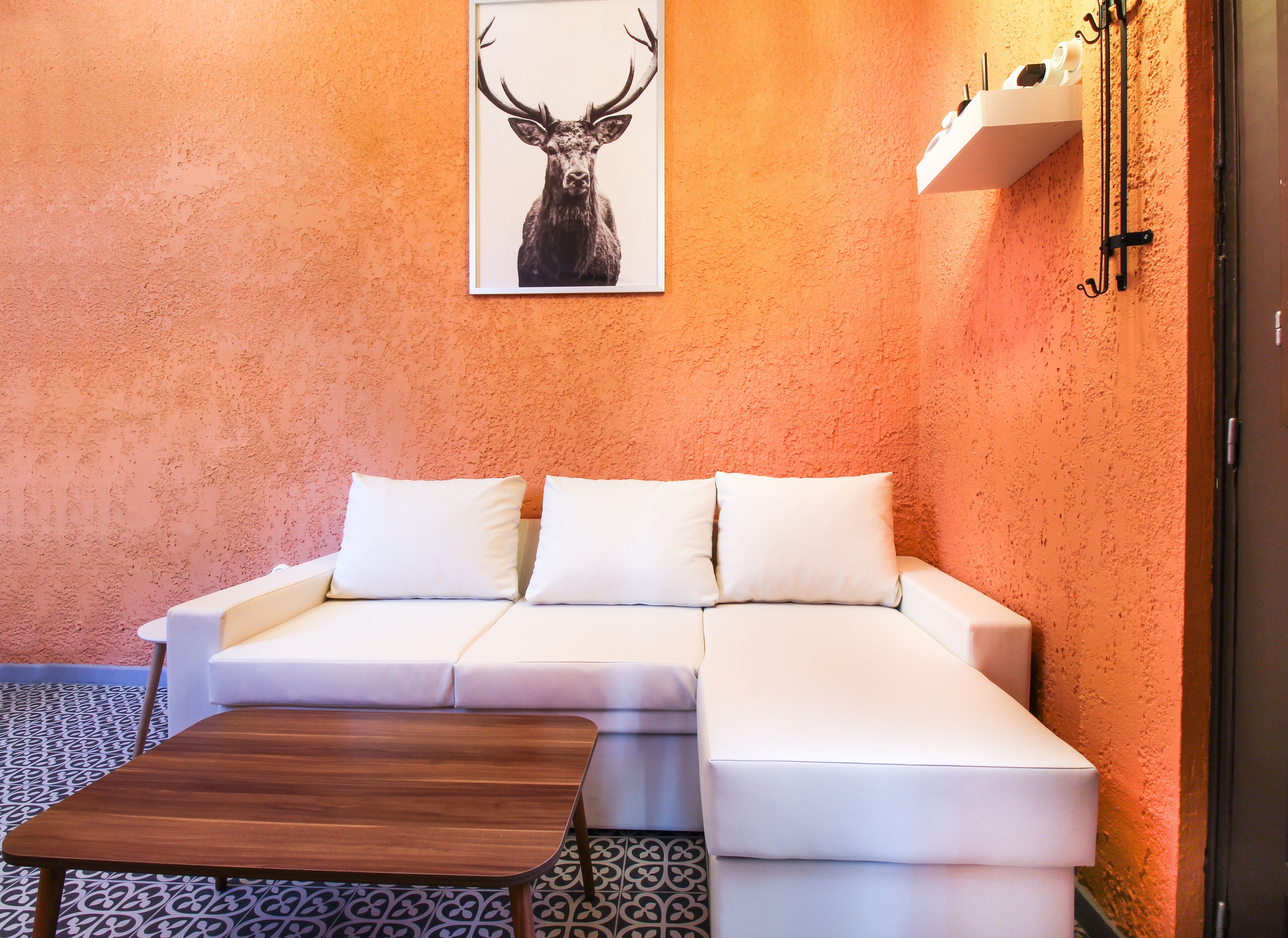 Une pièce moderne avec un canapé blanc, une table basse en bois et une œuvre d’art représentant une tête de cerf encadrée, le tout sur un mur orange à la texture particulière.