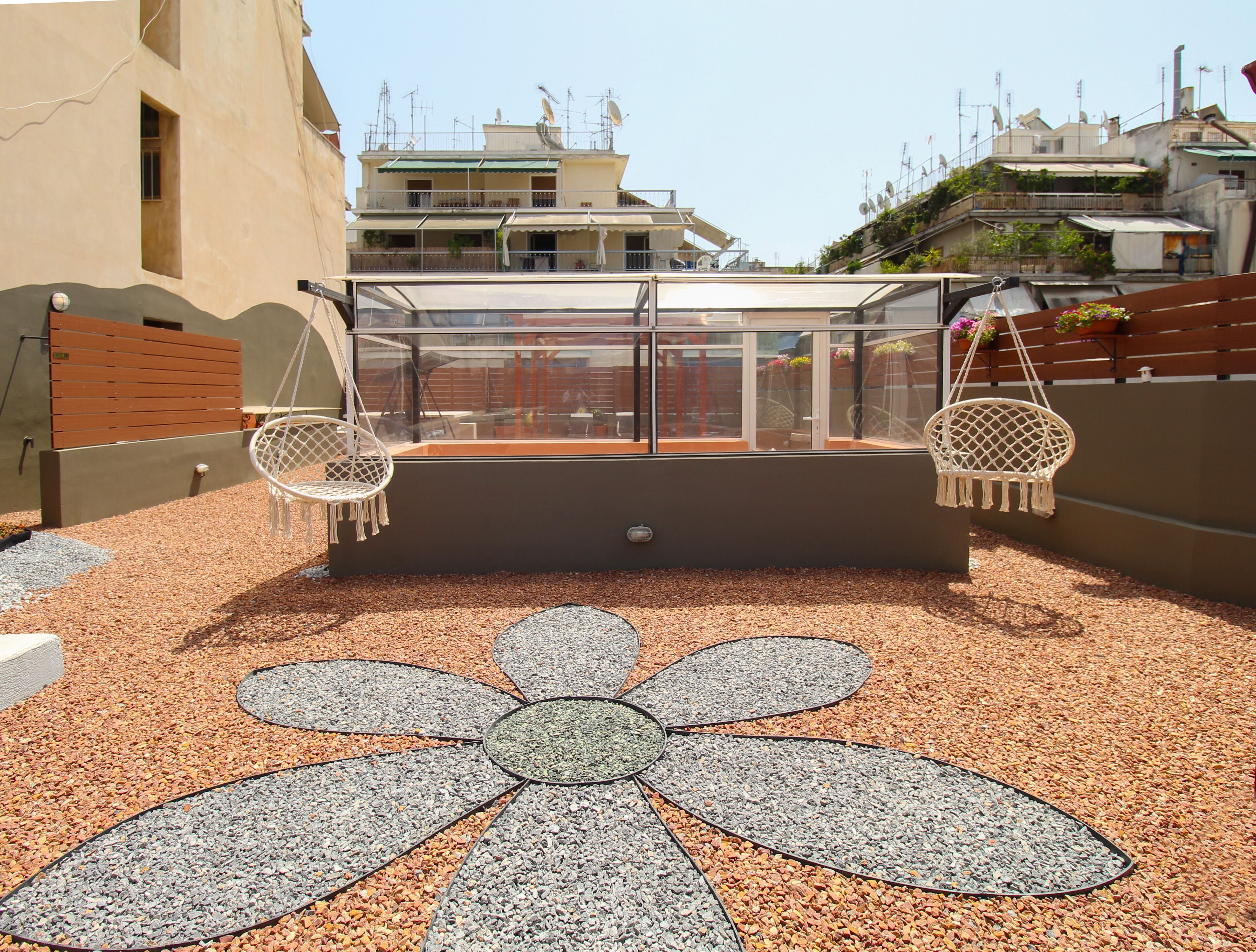 Une terrasse sur le toit dotée d’une balustrade en verre, de deux fauteuils suspendus et d’un chemin décoratif orné de motifs floraux.