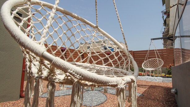 A macrame hanging chair in an outdoor area with a building in the background. - Modern apartment with roof terrace in Athens (Athens)