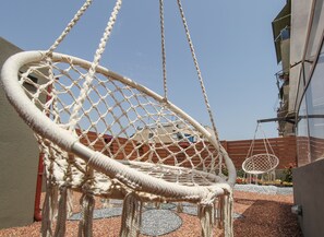 Een macramé hangstoel in een buitengebied, met een gebouw op de achtergrond.
