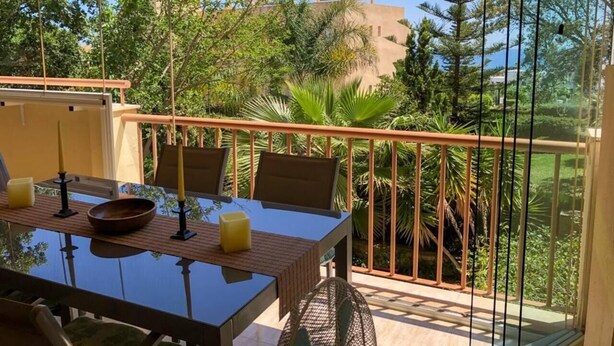 An outdoor dining area with a table, chairs, and a railing overlooking a garden and buildings. - Flat Sleeps 4 with Pool and Terrace (mijas costa)