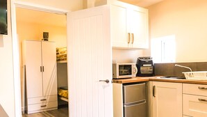 Eine kleine Küche mit weißen Schränken, einer Mikrowelle, einem Toaster und einem Kühlschrank.