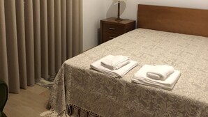 Ein ordentlich bezogenes Bett mit gefalteten Handtüchern, einer Nachttischlampe und einem Holfnachtkästchen in einem Hotelzimmer.