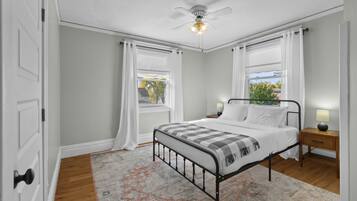 A bedroom with a bed, nightstands, a ceiling fan, and windows with curtains.
