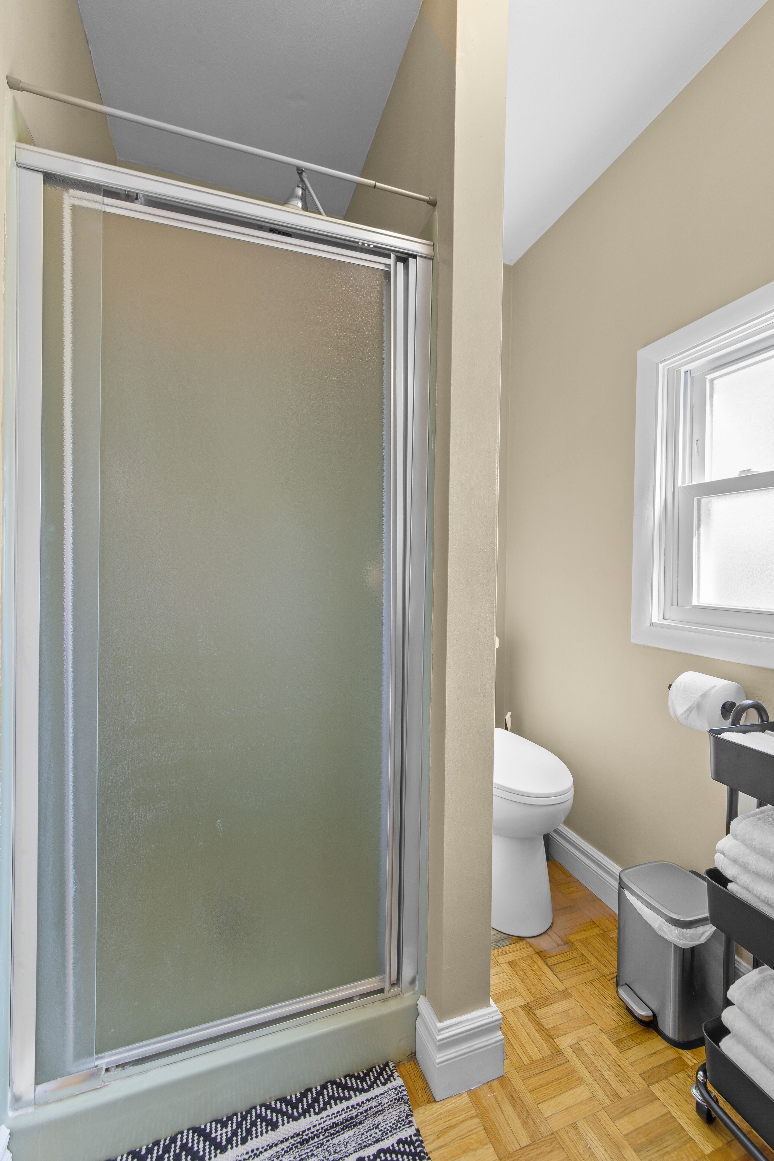 Een badkamer met een douchecabine van glas, een toilet, een prullenbak en een handdoekhouder.