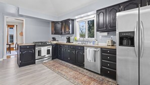 A modern kitchen with dark cabinets, stainless steel appliances, and a large window.