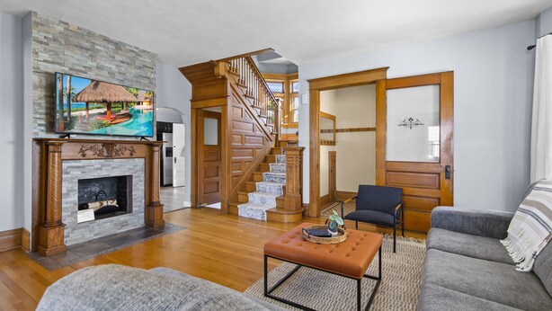 A spacious living room with a fireplace, a staircase, and a large window.