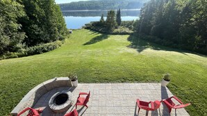 Eine Terrasse mit einem Steinkamin, roten Stühlen und Blick auf einen von Bäumen umgebenen See.