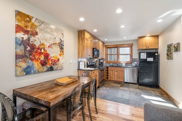 A modern kitchen with wooden cabinets, stainless steel appliances, and a dining area with a wooden table and chairs.