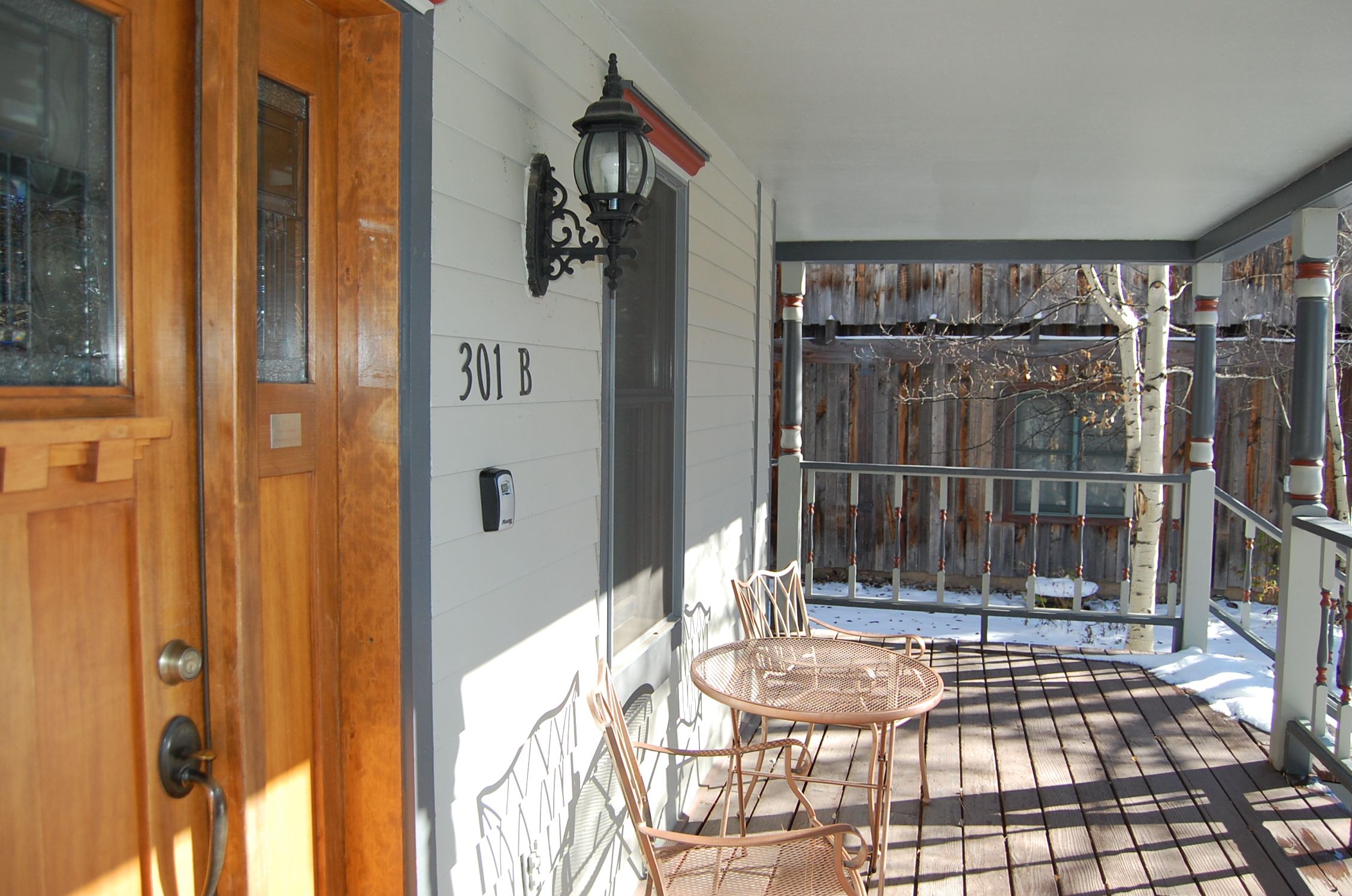 A wooden door with a number plate, a metal gate, and a small table with chairs on a wooden deck.