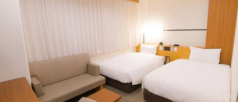 Habitación de hotel con dos camas, un sofá, una mesita y una lámpara.