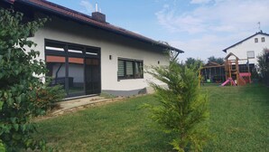 Une maison moderne dotée d’une grande porte vitrée, d’un petit jardin et d’une aire de jeux dans la cour.