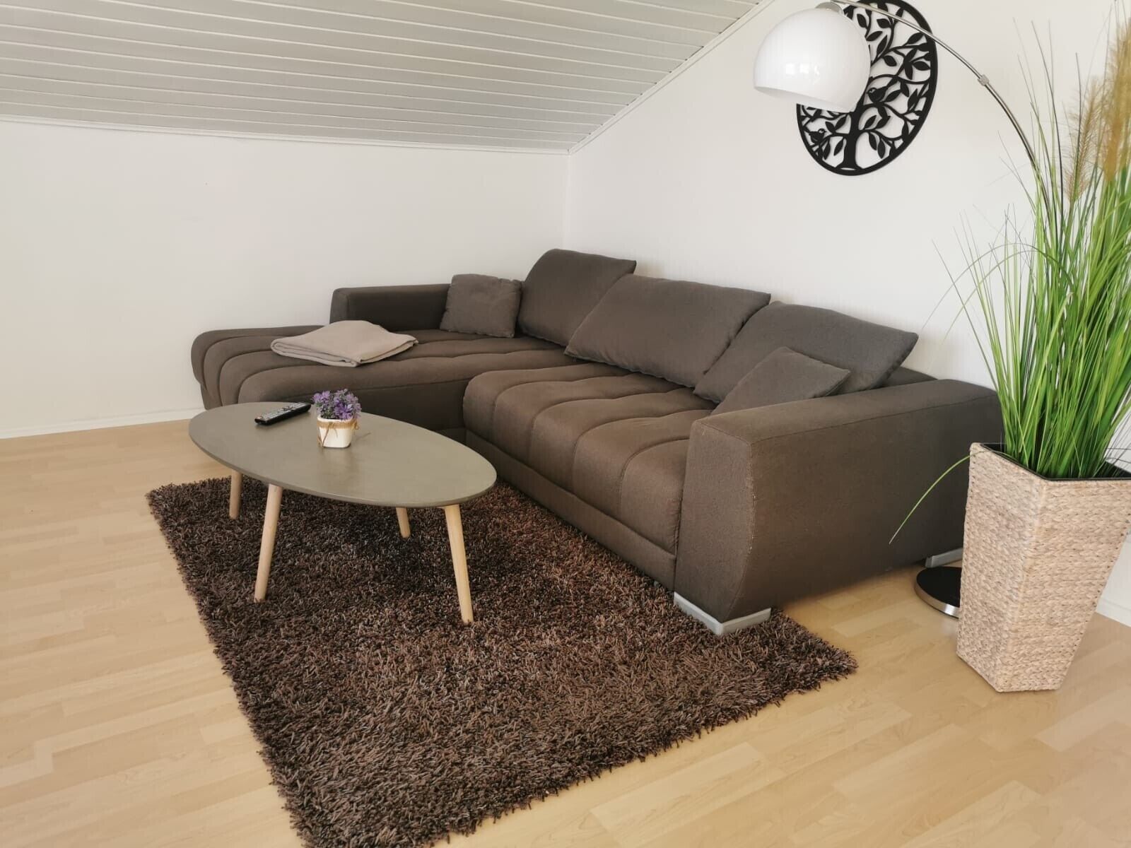 Ein modernes Wohnzimmer mit einer braunen Couch, einem runden Couchtisch, einer kleinen Pflanze und einem Wanddekor.