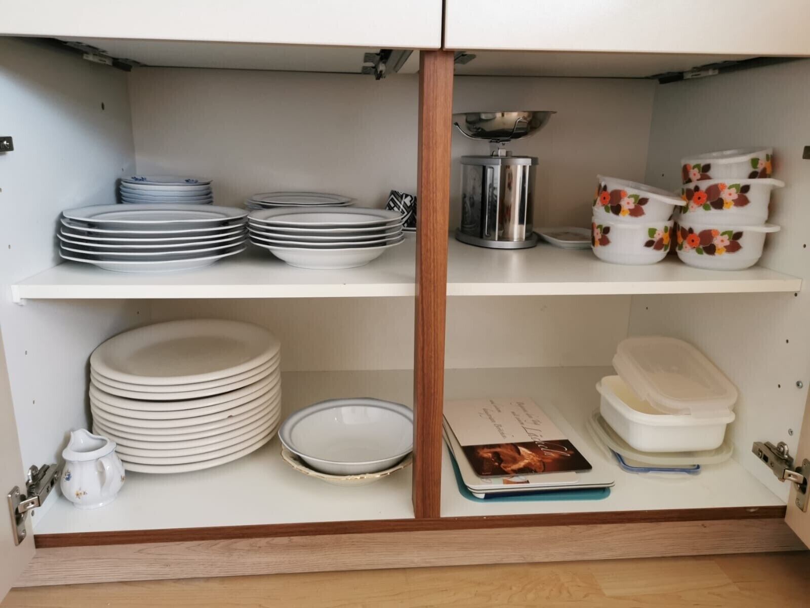 Eine Küchenschrank mit mehreren Einlegeböden, auf denen Teller, Schüsseln, ein Wasserkocher und ein Kochbuch stehen.