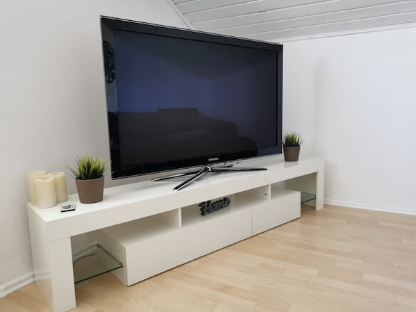 Un televisor de pantalla plana sobre un mueble blanco con un estante de vidrio debajo.
