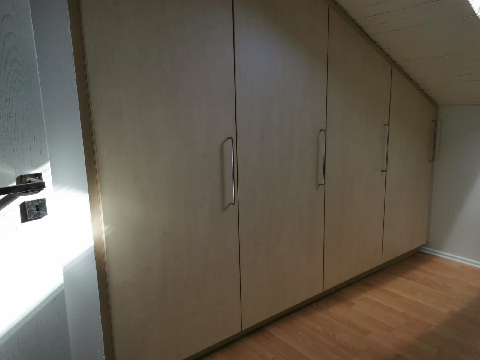 Ein Zimmer mit großem Kleiderschrank, Holzboden und schräg verlaufender Decke.