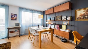 Ein modernes Wohnzimmer mit Essbereich, Holzmöbeln und einem Bücherregal mit verschiedenen Gegenständen.