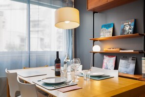 Una tavola imbandita con piatti, posate, bicchieri e una bottiglia di vino, con una lampada sopra e scaffali pieni di libri sullo sfondo.