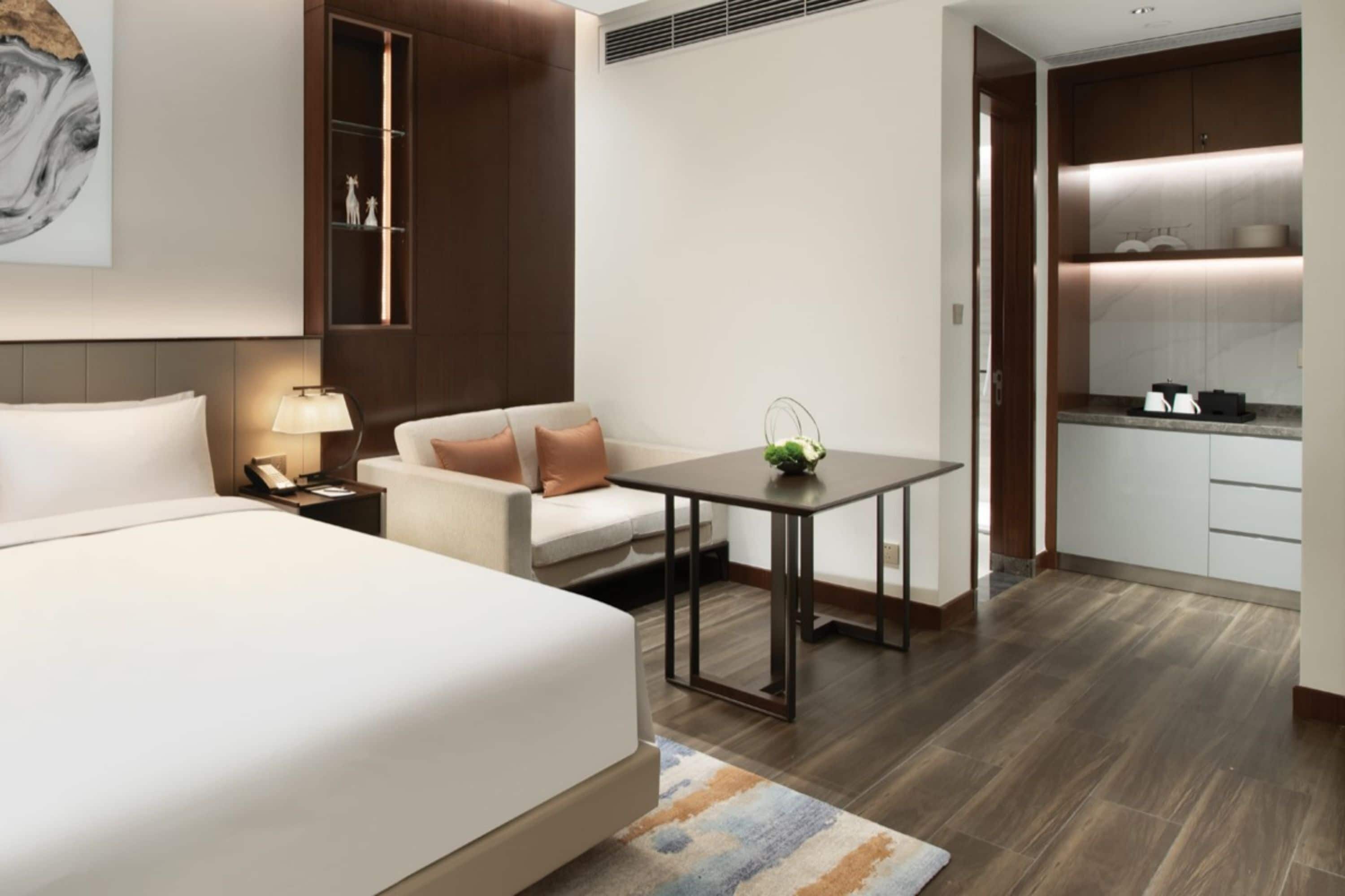 Een moderne hotelkamer met een groot bed, een bank, een klein tafeltje en een kitchenette.