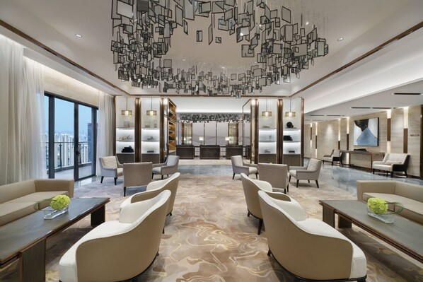 Een moderne hotellobby met een centraal zitgedeelte, een receptiebalie en een groot raam met uitzicht over de stad.