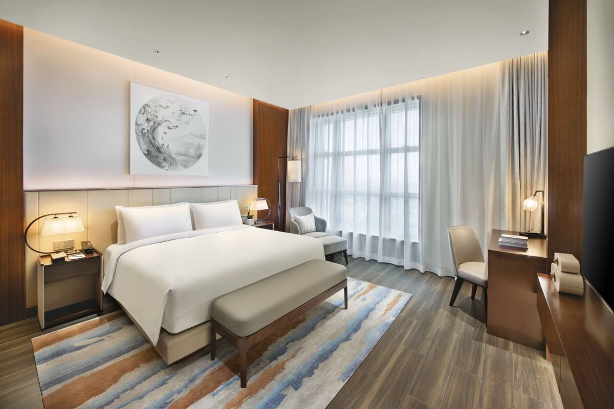 A modern hotel room with a large bed, a desk, a chair, and a television.