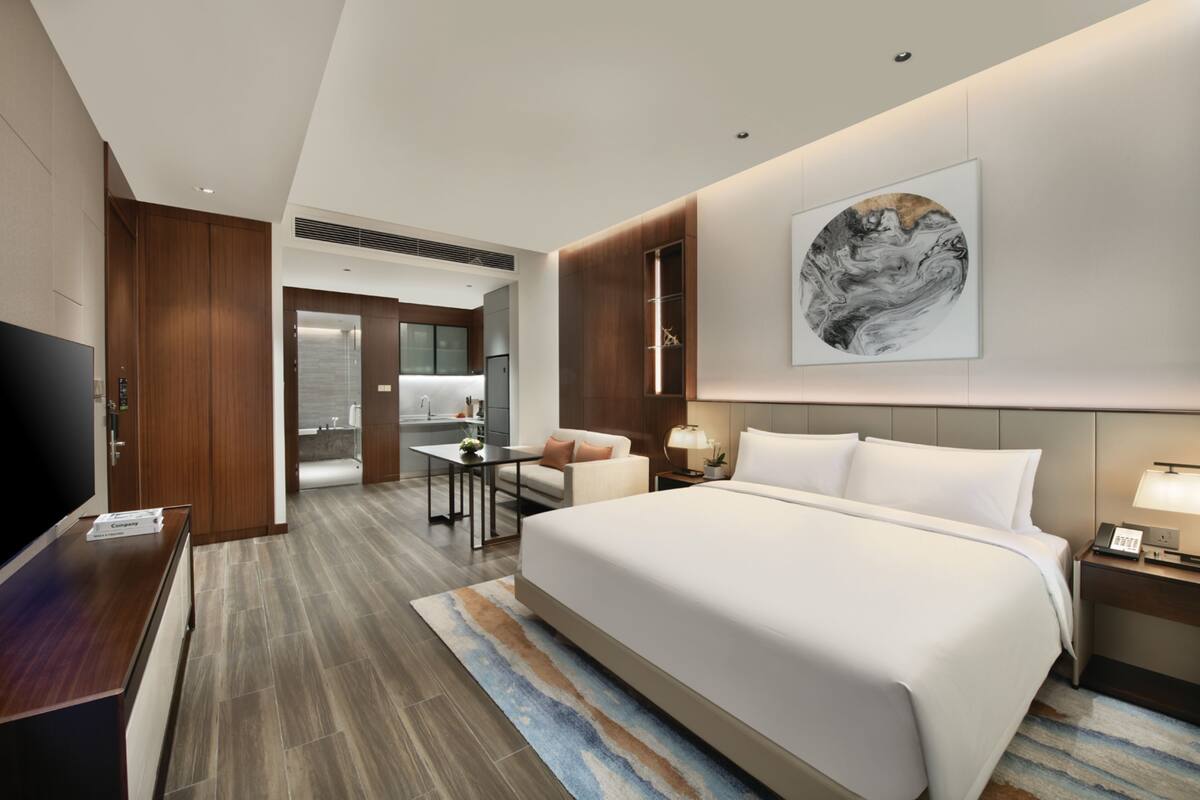A hotel room with a large bed, a desk, a chair, a TV, a bathroom, and a painting on the wall.