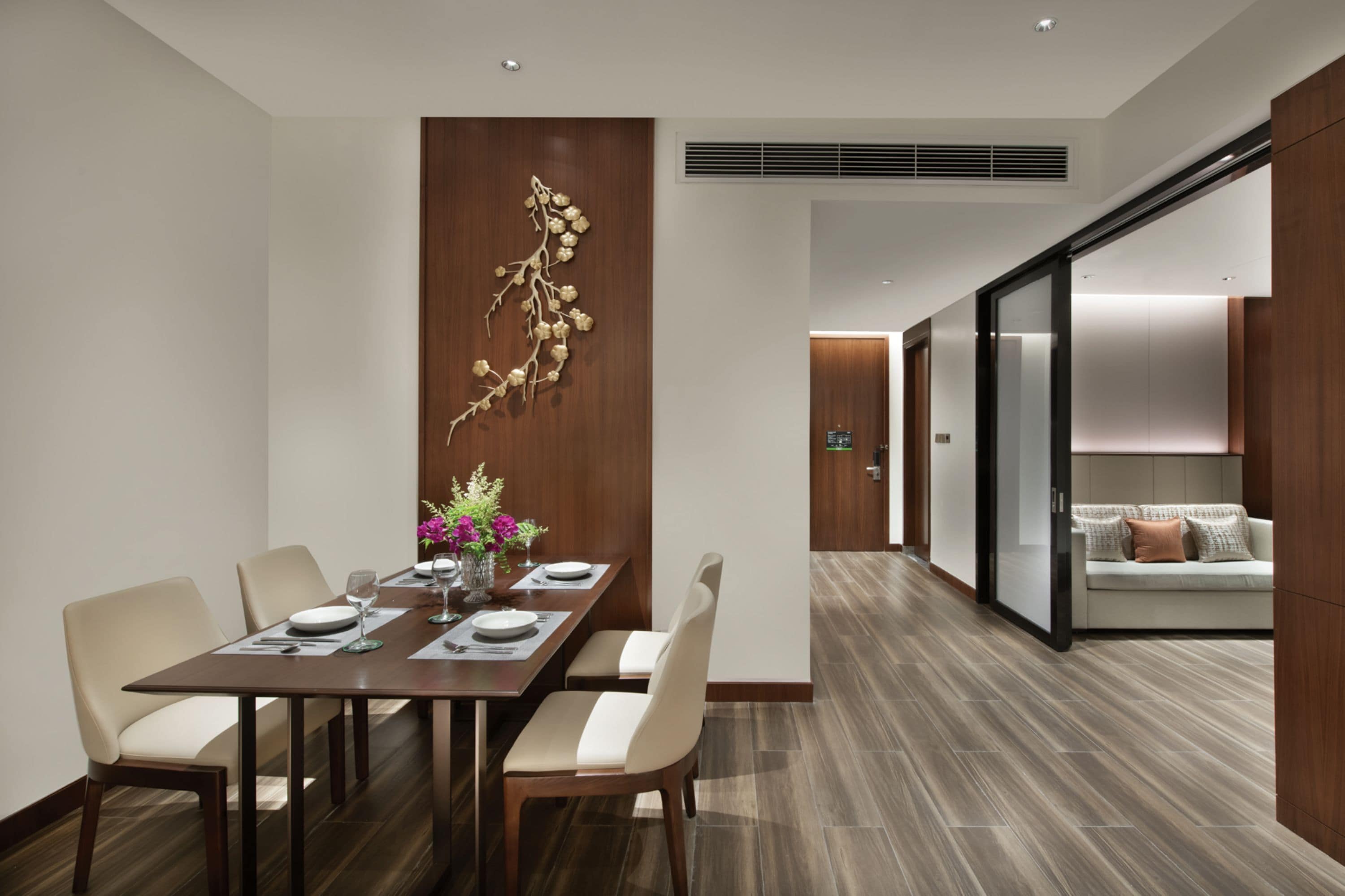 Een moderne eethoek met een houten tafel voor vier personen, een decoratief kunstwerk en een schuifdeur naar een woonruimte.
