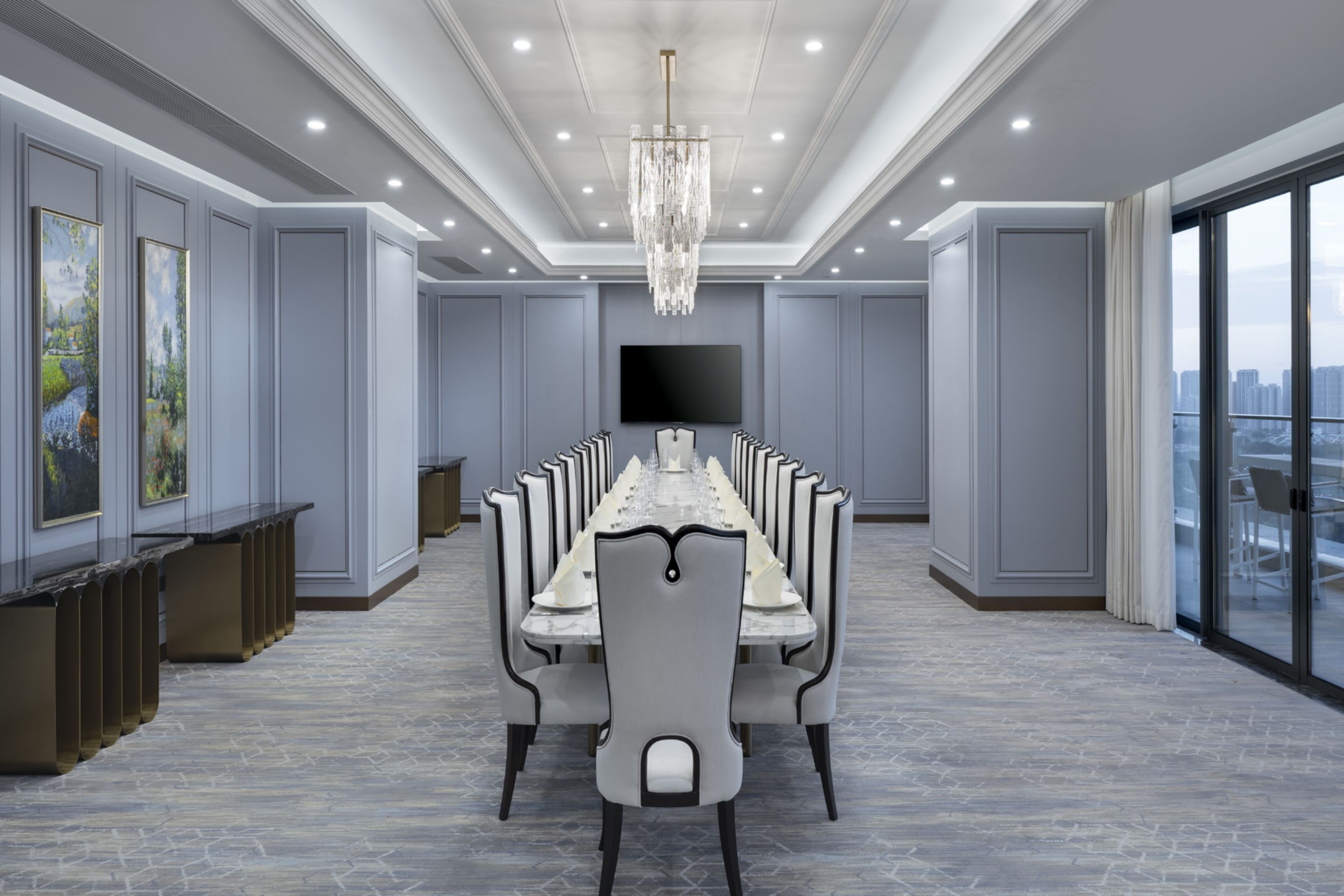 A conference room with a long table, chairs, a chandelier, a flat-screen TV, and a city view through large windows.